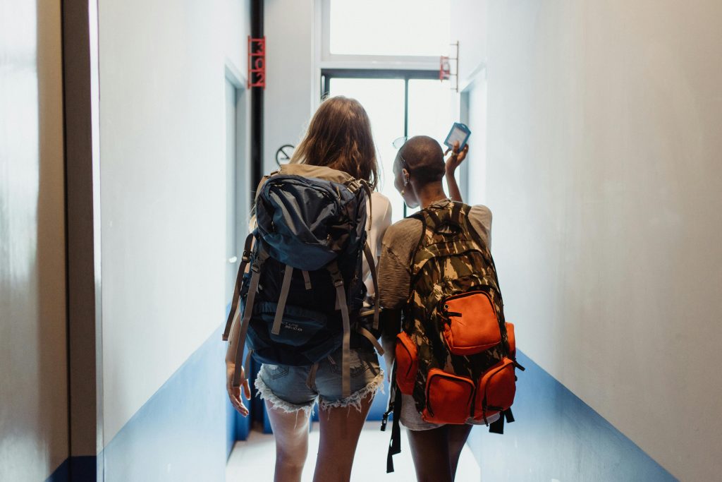 Two women with backpacks walking through a hallway, suggesting travel friendship.