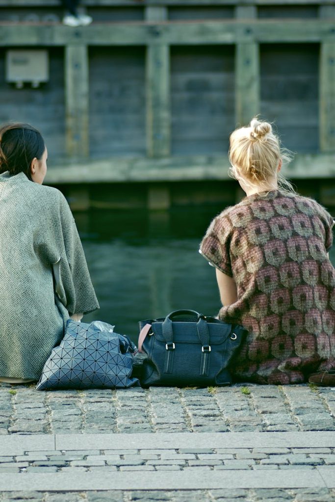 Two women sit along a canal in Copenhagen, Denmark, enjoying a serene moment by the water.