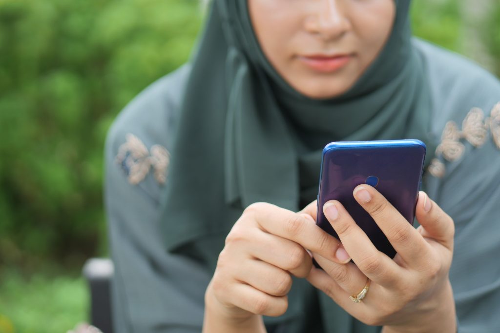 Close-up of a woman in hijab using a smartphone outdoors. Focus on hands and phone.